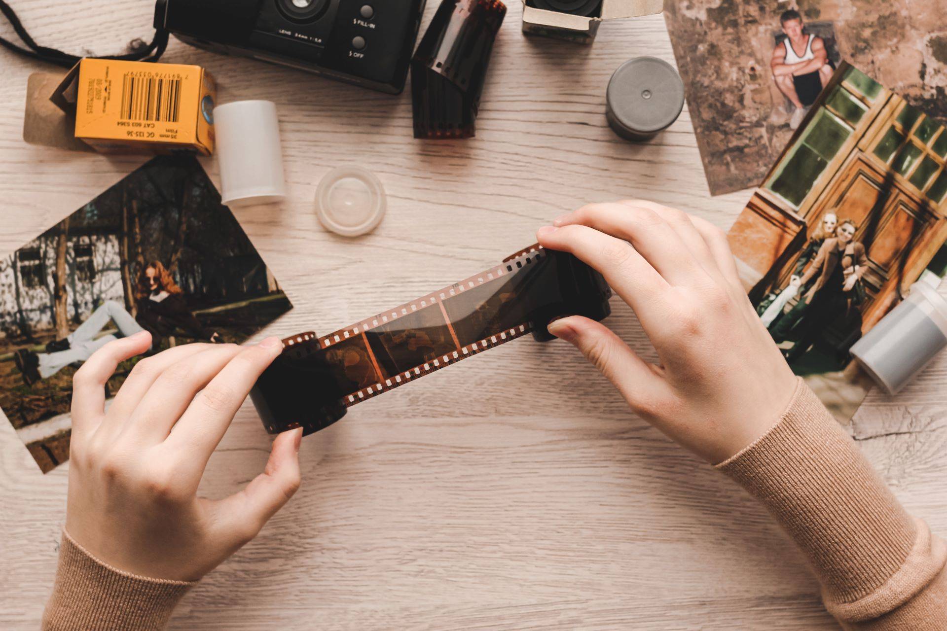 Hände halten ein Fotonegativ, umgeben von Fotografieausrüstung und alten Abzügen, als Symbol für den Prozess des Negative digitalisierens zur Bewahrung wertvoller Erinnerungen.