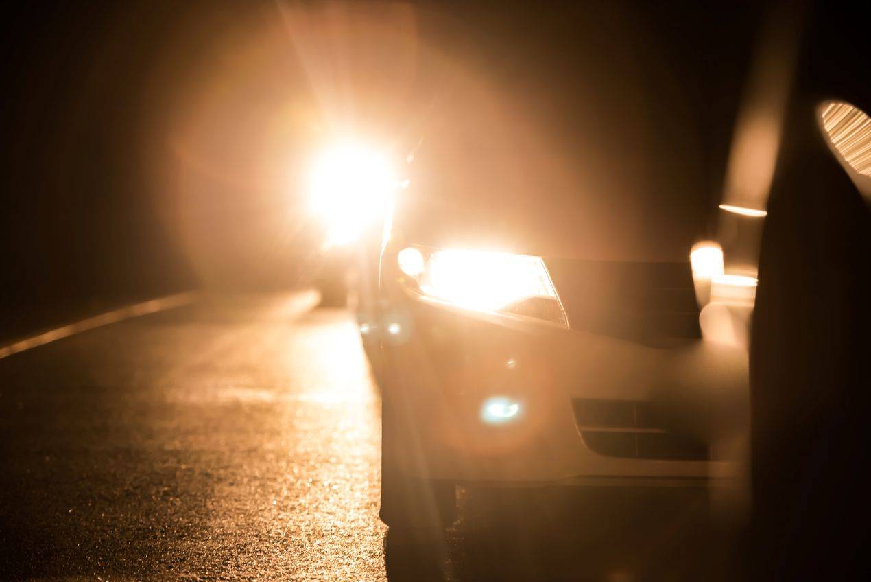 Fahrzeugbeleuchtung bei Dunkelheit mit starker Blendung durch Fernlicht im Gegenverkehr auf Landstrasse