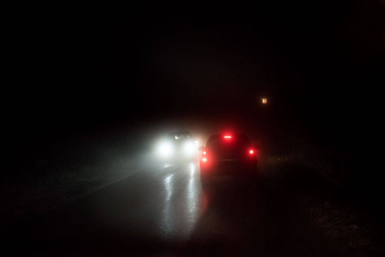 Fahrzeugbeleuchtung bei Nacht und Nebel mit eingeschaltetem Abblendlicht auf regennasser Landstrasse