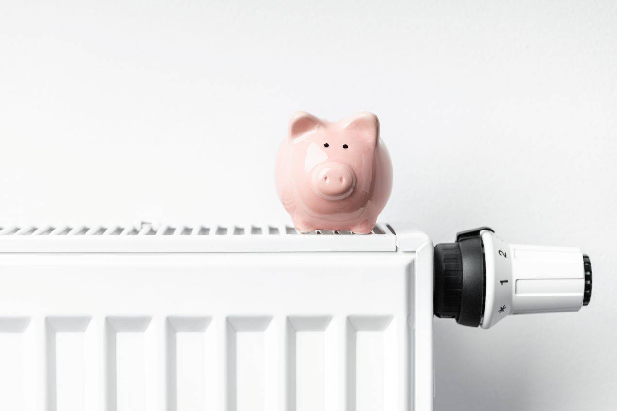 Sparschwein auf Heizkoerper als Symbol fuer Heizkostenersparnis und Einfluss steigender Heizölpreise Essen auf Haushaltsbudgets